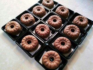 Top view of several mini bundt cakes neatly arranged in individual black plastic containers. Box of...