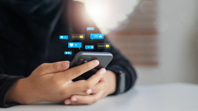 Close-up of a hand holding a smartphone with floating social media notifications including likes, comments, messages, and user reactions. Concept of digital engagement and online presence.