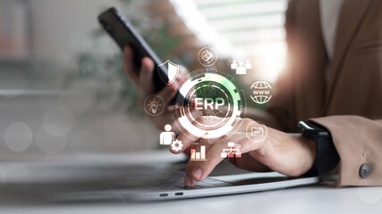 Businessperson using laptop and smartphone with ERP system interface and enterprise software icons. Concept of resource planning, business automation, and digital workflow.