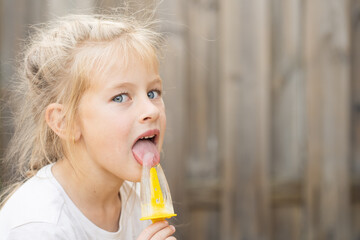 A young girl experiences the simple pleasure of a melting ice pop on a hot summer afternoon. Ideal for promoting summer products and happy family moments.