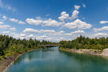 Turquoise river flowing under a bridge, surrounded by lush green forest and blue sky with clouds. Scenic nature landscape perfect for travel, outdoor, and environmental themes
