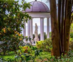 A statue in a gazebo in a park among greenery on a summer day.