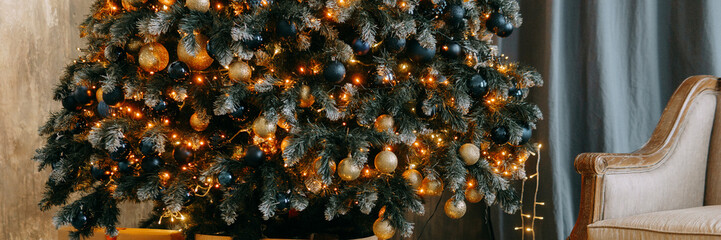 Decorated Christmas tree with shiny golden and blue ornaments, bright lights, and gifts below. Holiday season interior decor with cozy sofa.