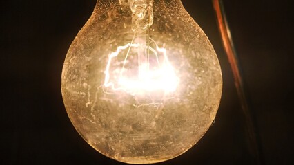 Close-up shot of a lit incandescent light bulb. The warm glow contrasts against a dark background,...