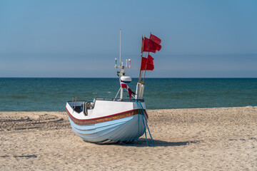 Traditional fishing boat with red flags on the sandy beach at Stenbjerg, North Jutland, Denmark. Calm North Sea and blue sky in a classic Danish coastal scene.