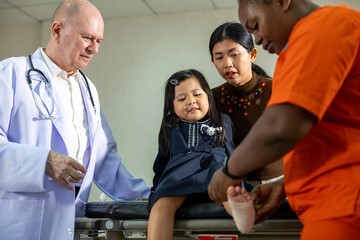 Little asian girl having accident with ankle sprain gets treatment from nurse and senior doctor in...