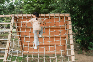 Child Climbing a Vertical Playground Net in a Park Surrounded by Lush Green Trees on a Sunny Day, Joyful Outdoor Activity for Kids