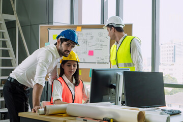 Group of engineers wearing safety helmets and vests analyzing building plans on computer in modern...