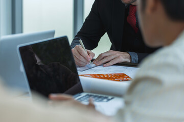 Hands of architect drawing on blueprint with orange template, surrounded by colleagues discussing project ideas on laptop. Concept of teamwork and technical design.
