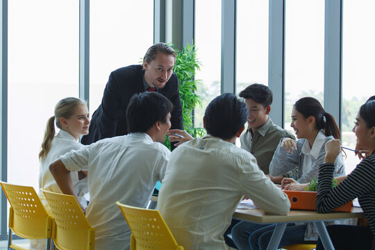 Group of Southeast Asian and Caucasian colleagues in business meeting, discussing strategy in modern office with natural light through glass windows.