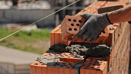 Bricklayer building wall with red bricks. Close-up of a construction worker laying red bricks with...