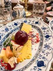 Colorful dessert presentation featuring a creamy yellow mousse, vibrant fruits, and decorative elements on an elegant blue and white porcelain plate, showcasing culinary artistry and indulgence