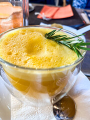 Sea buckthorn drink in a clear cup, topped with yellow foam and garnished with fresh herbs, showcasing a vibrant and healthy winter beverage experience