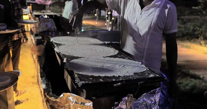 Indian caterers preparing fresh uttapam and crispy dosa on a hot tawa during a live food counter at a festive event
