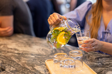 Woman pouring summer refreshing homemade chilled drink with mint and citrus and ice. Nonalcoholic iced tea, lemonade with lemon. Chilled water with herbs