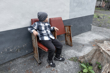 Little boy in a checkered shirt sits on vintage chairs with brown leather seats