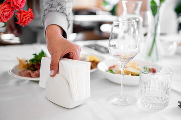 Elegant dining table setup with a hand picking a napkin from a white holder, surrounded by plates,...