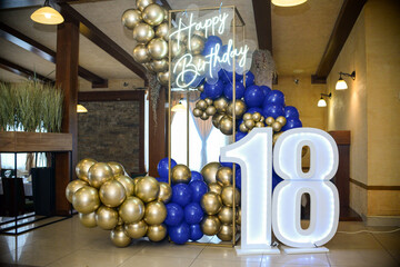Decoration of blue and yellow balloons. A neon sign that says Happy Birthday in English and a large...