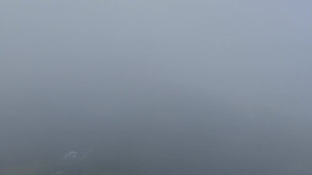 Emerging from fog over coastal farms and houses by rocky beach and blue ocean