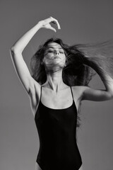 black and white woman in black leotard dancing gracefully with flowing hair against plain...