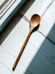Wooden spoon with smooth surface and round bowl placed diagonally on cracked light-gray background, evoking rustic charm and simplicity