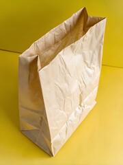 Crinkled brown paper bag standing upright on vibrant yellow surface against matching yellow background, evoking utilitarian warmth and minimalism