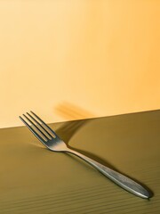 Silver metallic fork diagonally placed on yellow ridged surface under natural light, casting sharp shadow and evoking bold minimalism