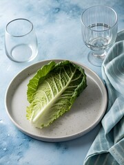 Single savoy cabbage leaf on white ceramic plate with empty glasses and striped cloth — evoking rustic purity and seasonal freshness