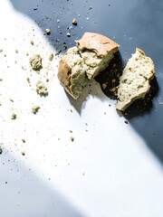 Broken loaf of crusty bread with scattered crumbs on dual-tone background — evoking rustic simplicity and textural food narrative