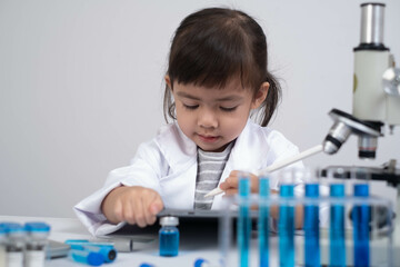 A young child in a lab coat conducts experiments with a microscope and test tubes, showcasing...