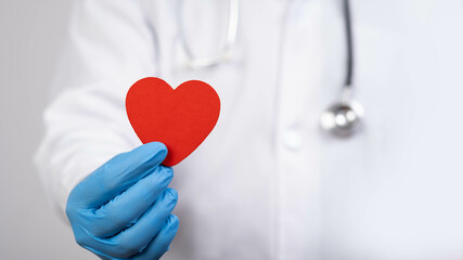 A healthcare professional in a white coat holds a red heart symbol, emphasizing compassion and care...