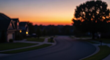 Blurred suburban street at sunset with houses and tree silhouette against colorful sky