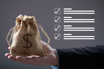 A hand holds a small money bag while checkboxes appear in the background, symbolizing finance and...