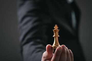 A hand holds a golden chess king piece, symbolizing strategy and leadership in a dark, elegant...