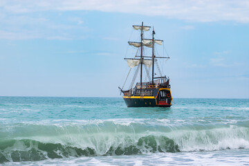 Seascape with a sailing ship stylized as a pirate. Wave in the foreground