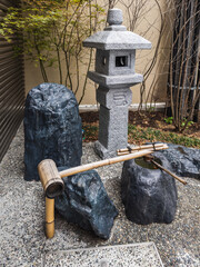 Serene Japanese garden scene featuring a stone lantern, tsukubai (water basin), and bamboo dipper. ...