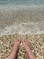 Bare Feet on Pebble Beach Touching Sea Foam on Sunny Summer Day at Shoreline