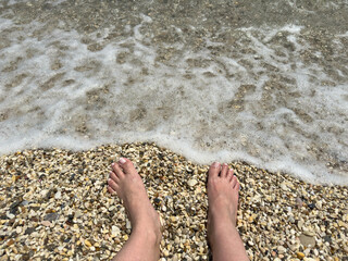 Bare Feet on Pebble Beach Touching Sea Foam on Sunny Summer Day at Shoreline