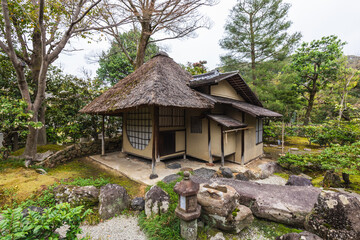 Traditional Japanese house with thatched roof nestled in a serene garden.  Stone pathway, lantern,...