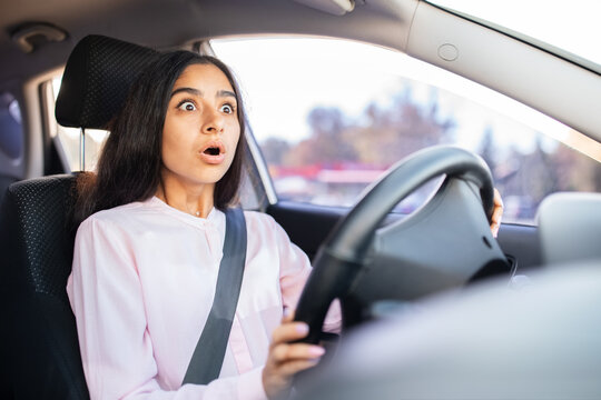 Shocked Indian woman driver looking ahead in fear, gripping steering wheel tightly. Illustrates sudden danger, panic or unexpected road situation inside car, closeup