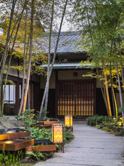 Tranquil Japanese garden path at dusk, illuminated lanterns lead to a traditional house with shoji...