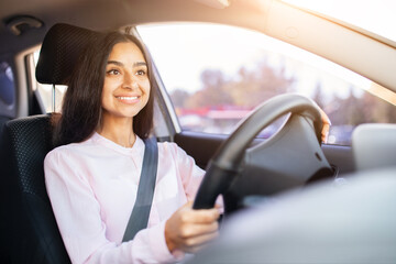 Young Indian woman smiling confidently while driving car, looking ahead with hands on the steering wheel. Safe, happy, relaxed and focused female driver lifestyle concept