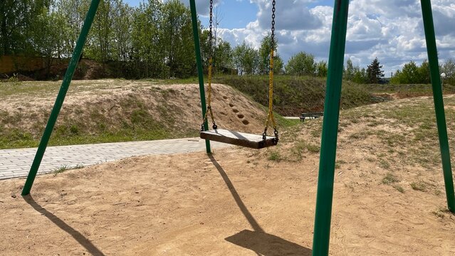 A swing set sits on a sandy playground area under a partly cloudy sky.