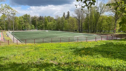 Obraz premium A grassy park area with a soccer field enclosed by a metal fence is visible.