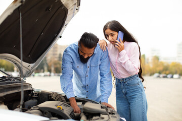 Indian woman calling to repairment station while man trying to fix car engine. Woman places...