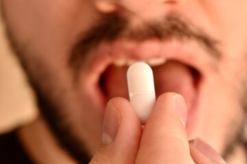 Man taking a pill. Close-up of male hand placing tablet in mouth. Concept of medicine, treatment,...