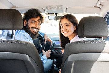 Happy Indian couple turning in car and smiling toward camera from front seats. Represents...