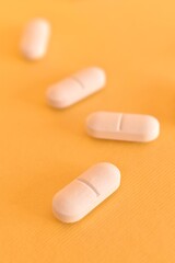 Close-up of white medical tablets on a bright yellow surface. Concept of medicine, pharmacy, and...