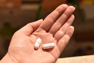 Female hand holding two white pills. Concept of medical treatment, healthcare, and pharmaceutical medication.