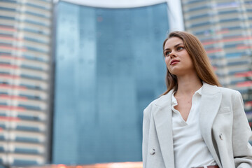 Young woman in white coat looking confident with urban skyscraper background, fashion style,...